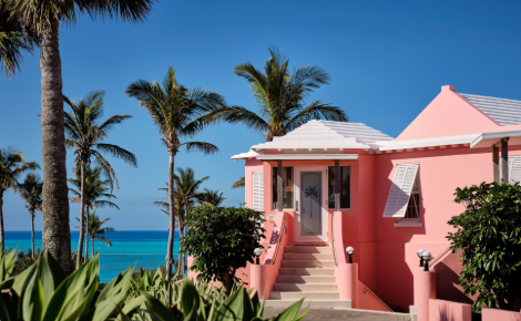 Pink Bermuda cottage surrounded by palm trees overlooking the turquoise ocean at Cambridge Beaches Resort.
