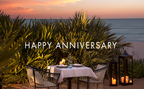 Gift card image of a table set for two on the beach at sunset with the text “Happy Anniversary