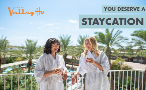two women in robes on hotel room balcony with sparkling wine; text says "You Deserve a Staycation"