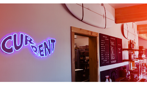 bar area of the current cafe with current sign in neon blue and surfboard above the door.