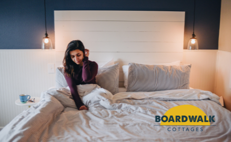 woman with long black hair wearing purple shirt sitting up in bed with boardwalk cottages logo in lower right corner