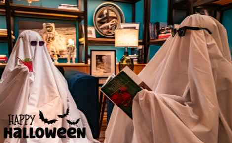 Image of bed sheet ghosts enjoying a festive cocktail and reading in the Ames Library at the Ameswell Hotel, with the words "Happy Halloween"