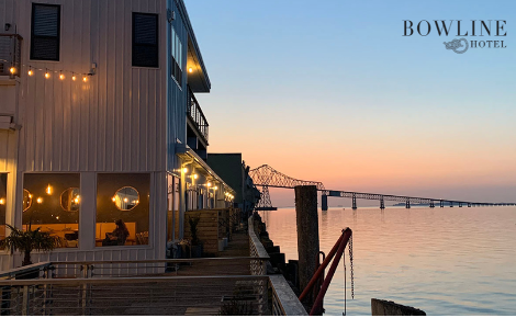 A pastel sunset behind the Astoria-Megler bridge and columbia river is in the background. The left  hand side boasts the Bowline hotel. The bowline hotel logo is in the top right corner.