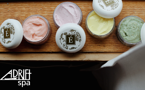 Four small pastel skincare jars are opened in an arial view. There's an E logo on the lids, and the Adrift Spa logo is in the bottom left corner.