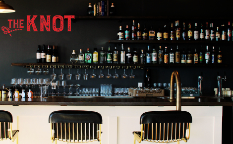 the knot logo is in red in the upper left corner, it shows a bar top and spirits in the background.