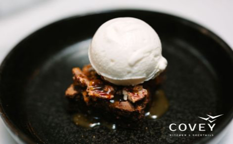 Vanilla ice creams sits on top of a warm brownie. This image is promoting Covey Kitchen + Cocktails. 